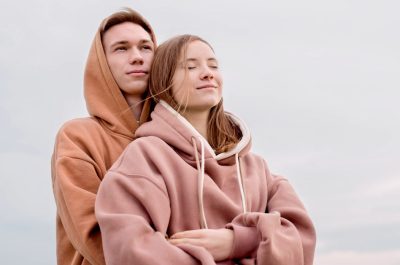 Happy young loving couple wearing hoods embracing each other outdoors in the park